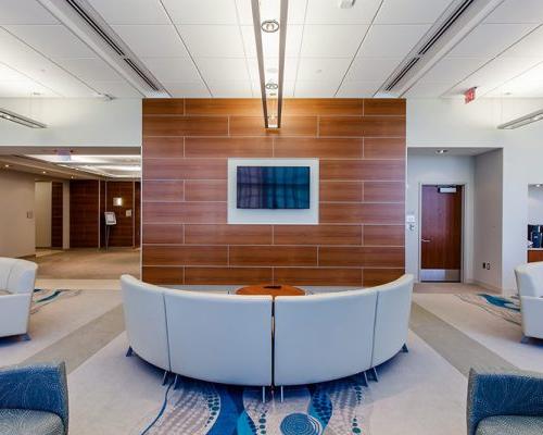 Interior photo of a lounge with cream colored couches in front of wood paneled wall with a television.